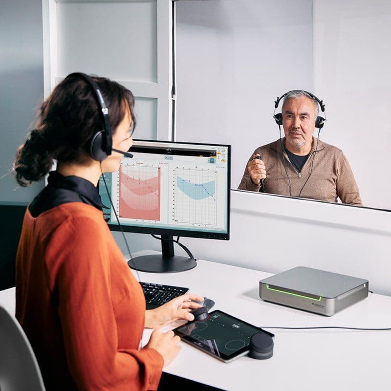 An elderly man is undergoing an audiometric test while the audiologist is using the touch keyboard